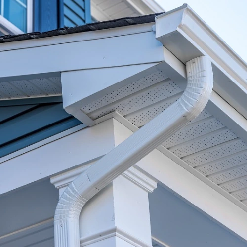 White downspout connected to matching eavestroughs, fascia and vented soffit beside blue siding